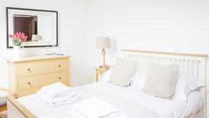 Een netjes ingerichte slaapkamer met een bed, een nachtkastje met een lamp, een kast en een spiegel.