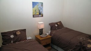 Un dormitorio con dos camas, una mesita de noche con lámpara y un cartel en la pared.