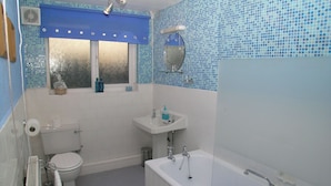 Un baño con inodoro, lavamanos, bañera y una ventana con cortina azul.
