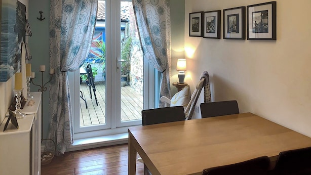 Un comedor con mesa y sillas de madera, vistas a un patio exterior a través de un ventanal y cuadros en la pared.