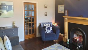 Una sala de estar con chimenea, un sillón azul, un sofá gris y una puerta de madera.