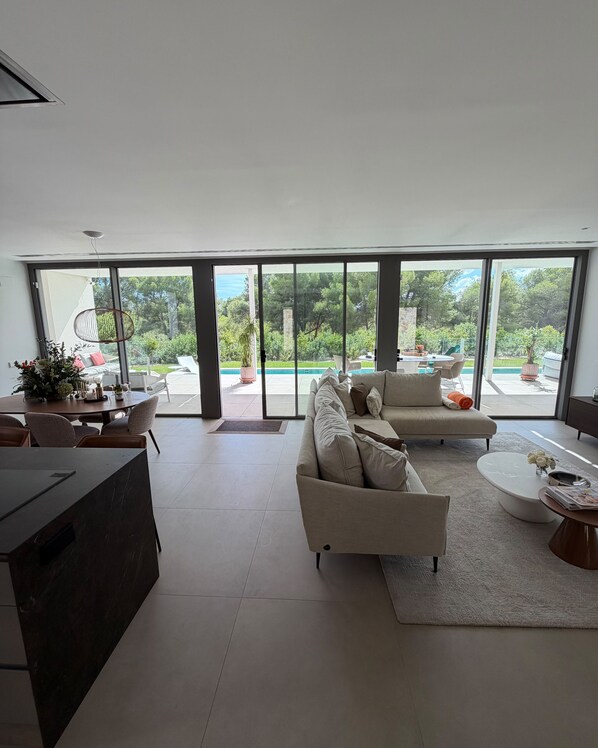 A spacious living area with a large window, a sofa, a coffee table, and a dining table.