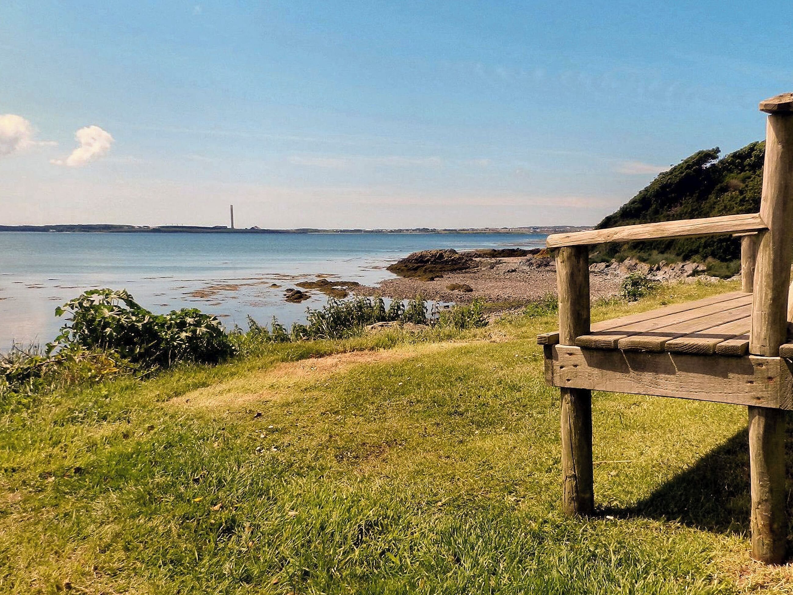 Una plataforma de madera con vistas a una zona costera, con un faro a lo lejos.