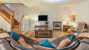 Un salon comprenant un ensemble de canapés, une table basse, une cheminée, un téléviseur et un escalier.