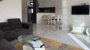 Un soggiorno moderno con un tavolino in vetro, un divano, una TV a parete e un'area pranzo con sedie e tavolo.