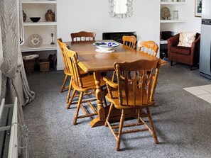 Un coin repas avec une table et des chaises en bois, un bol posé sur la table et des étagères ornées d’objets décoratifs.