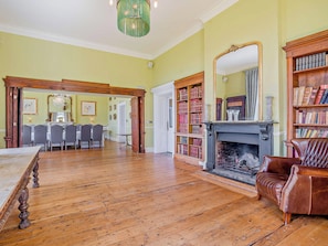 A spacious room with a wooden floor, a fireplace, a dining area with chairs, and a bookshelf filled with books.