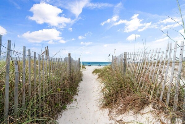 A sandy path leading to a beach with a wooden fence on either side.