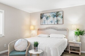 A bedroom with a bed, a chair, a bedside table, and a wall painting.