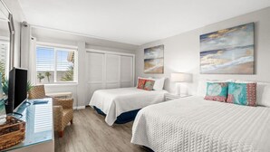 Habitación de hotel con dos camas, un televisor, un escritorio con ordenador y una ventana con persianas.