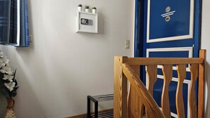 Een kamer met een houten stoel, een wit schap met een klok en een blauwe deur.