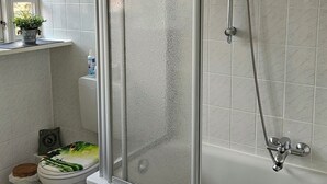 Een badkamer met een douche met glazen wand, een toilet met een groene mat en een handdoekhouder met een groene handdoek.