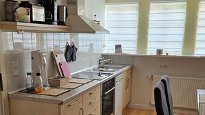 Een moderne keuken met een centraal eiland, ingebouwde apparatuur en een eethoek met een stoel.