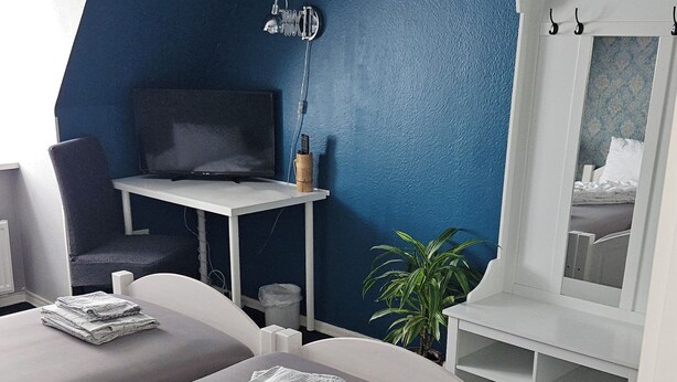 Een slaapkamer met twee bedden, een bureau, een televisie en een kast met haken.
