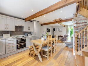A kitchen with wooden beams, a dining area with a table and chairs, and a staircase.