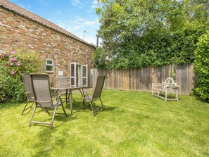 Un jardin avec un mur en briques, une clôture en bois et une table entourée de chaises.