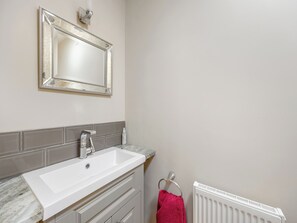 Un baño con un lavabo blanco, un espejo, un perchero con una toalla roja y un radiador blanco.