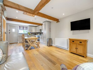 Une cuisine moderne avec des poutres en bois, un coin repas avec une table et des chaises, un canapé, un téléviseur fixé au mur et un radiateur.