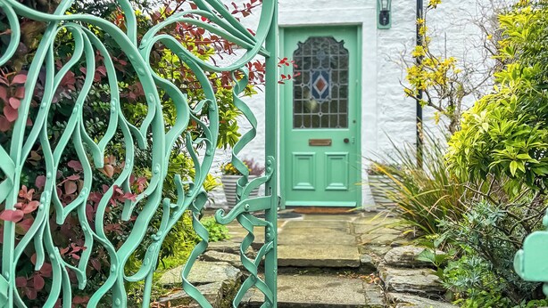 A green door with a decorative glass panel, a white wall, and a stone staircase leading to the entrance. - A perfect location for a family island break by the seaside. (Lochranza)