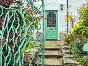Une porte verte ornée d’un panneau de verre décoratif, un mur blanc et un escalier en pierre menant à l’entrée.