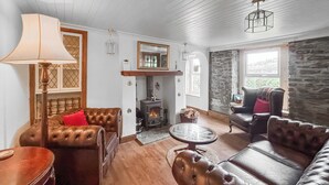 A cozy living room with leather sofas, a fireplace, and a stone wall. - A perfect location for a family island break by the seaside. (Lochranza)