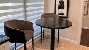 Et moderne køkken med et rundt spisebord, to stole og en flaske champagne i en ramme på væggen.