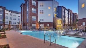 Ein modernes Apartmenthaus mit Schwimmbad, Liegestühlen und einer gepflegten Außenanlage.