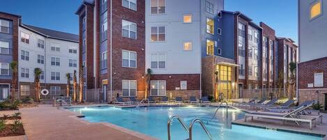 A modern apartment building with a swimming pool, lounge chairs, and a well-maintained outdoor area.