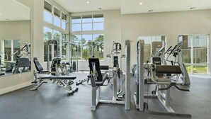 Ein geräumiger Fitnessraum mit verschiedenen Trainingsgeräten, großen Fenstern und einem Spiegel.