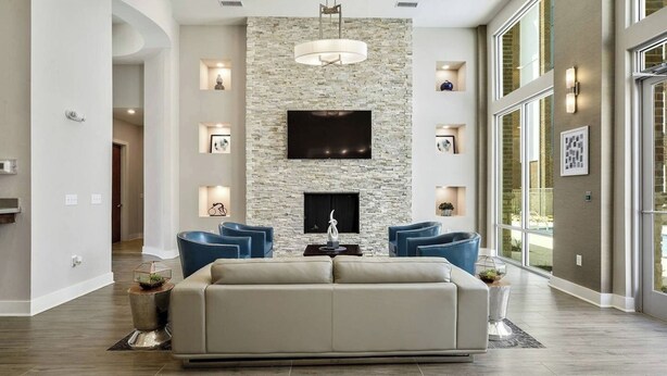 Ein großzügiges Wohnzimmer mit Steinwand, Flachbildfernseher und Kamin. Zwei blaue Sessel und ein beiges Sofa sind ebenfalls vorhanden.
