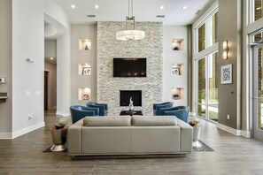 Un salon spacieux avec un mur d’accent en pierre, un téléviseur à écran plat et une cheminée. On y trouve deux fauteuils bleus et un canapé beige.