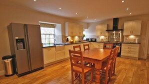 A modern kitchen with wooden flooring, a dining table with chairs, and built-in appliances.