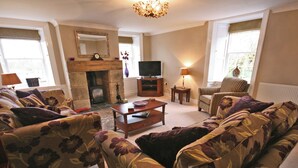 A living room with floral-patterned sofas, a fireplace, a television, and a lamp.
