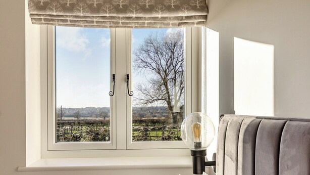 A bedroom with a window, a bedside lamp, and a view of a rural landscape.