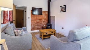 A living room with a brick fireplace, a television mounted on the wall, and two grey sofas.