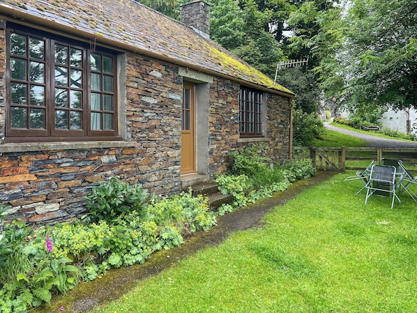 Ein Steinhaus mit Tür, Fenstern und einem grünen Garten mit Stühlen.