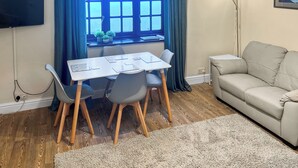 Een kamer met een eettafel, stoelen, een bank, een televisie en een raam met gordijnen.