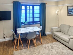 Una habitación con una mesa de comedor, sillas, un sofá, un televisor y una ventana con cortinas.