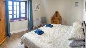 Een slaapkamer met een bed, een dressoir, een radiator, een stoel en een raam met gordijnen.