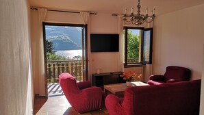 Ein Wohnzimmer mit Balkon, roten Sofas, einem Holztisch und einem Fernseher.