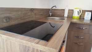 Eine moderne Küche mit einem schwarzen Induktionskochfeld, einer Edelstahl-Spüle, Holzschränken und einem Wasserkocher.
