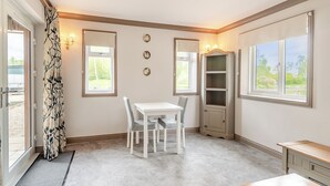 A room with a dining table, chairs, a cabinet, and a window with a view of greenery. - A peaceful location for a relaxing break with excellent fishing to enjoy. (Marston)