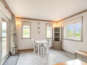 A room with a dining table, chairs, a cabinet, and a window with a view of greenery.