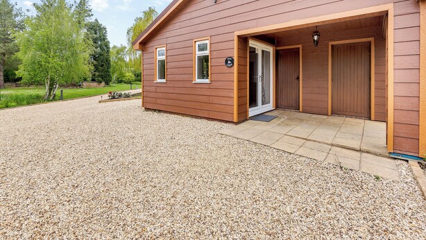 A wooden building with a gravel driveway, a covered entrance, and a door. - A peaceful location for a relaxing break with excellent fishing to enjoy. (Marston)