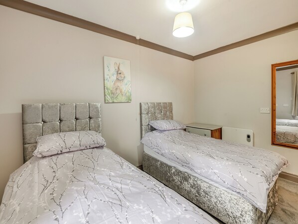 A bedroom with two beds, a bedside table, a mirror, and a painting on the wall.