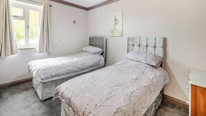 A bedroom with two beds, a window with curtains, a ceiling light, and a wall-mounted painting. - A peaceful location for a relaxing break with excellent fishing to enjoy. (Marston)
