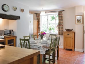 A dining area with a table set for four, a microwave, wooden chairs, a potted plant, and a window with curtains.