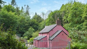A red building with a fenced yard, surrounded by dense green foliage.