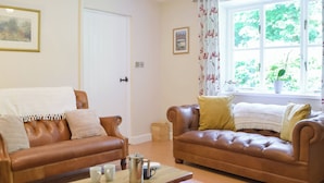A living room with two brown leather sofas, a wooden coffee table, and a window with a view of greenery.