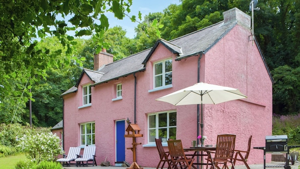 A pink house with a patio, a table with chairs, and a grill.